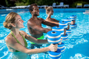 Three smiling people holding foam dumbbells in an outdoor pool. Three smiling people holding foam dumbbells in an outdoor pool.