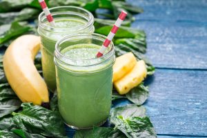 Deux bocaux remplis de smoothie vert entourés d’une banane, de morceaux d’ananas et d’épinards.