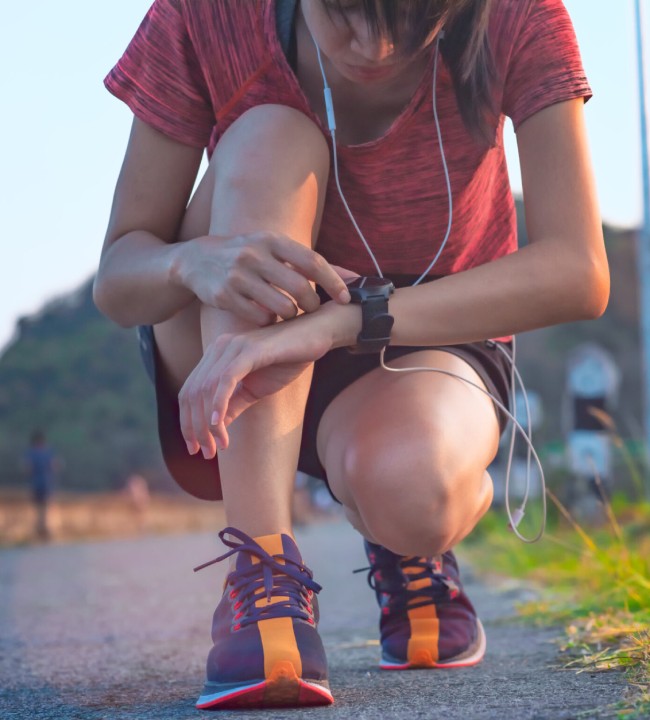 Young woman with earphones checking her tracks on her smartwatch outdoors
