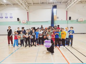 Une femme à genoux devant un groupe d’enfants tient une pancarte du défi Ensemble, on bouge de ParticipACTION dans le gymnase d’une école.
