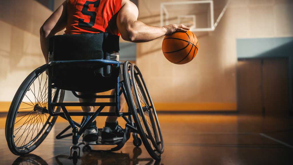 person in wheelchair on basketball court bouncing a basketball