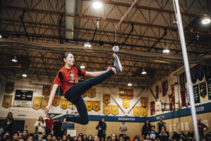 A girl playing the Inuit game called one-foot high kick in a gymnasium.
