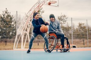 Un homme en fauteuil roulant joue au basket avec une femme debout. Un homme en fauteuil roulant joue au basket avec une femme debout.