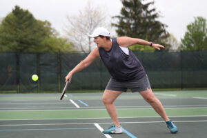 A person playing pickleball on an outdoor tennis court. A person playing pickleball, a so-called fitness fad, on an outdoor tennis court.