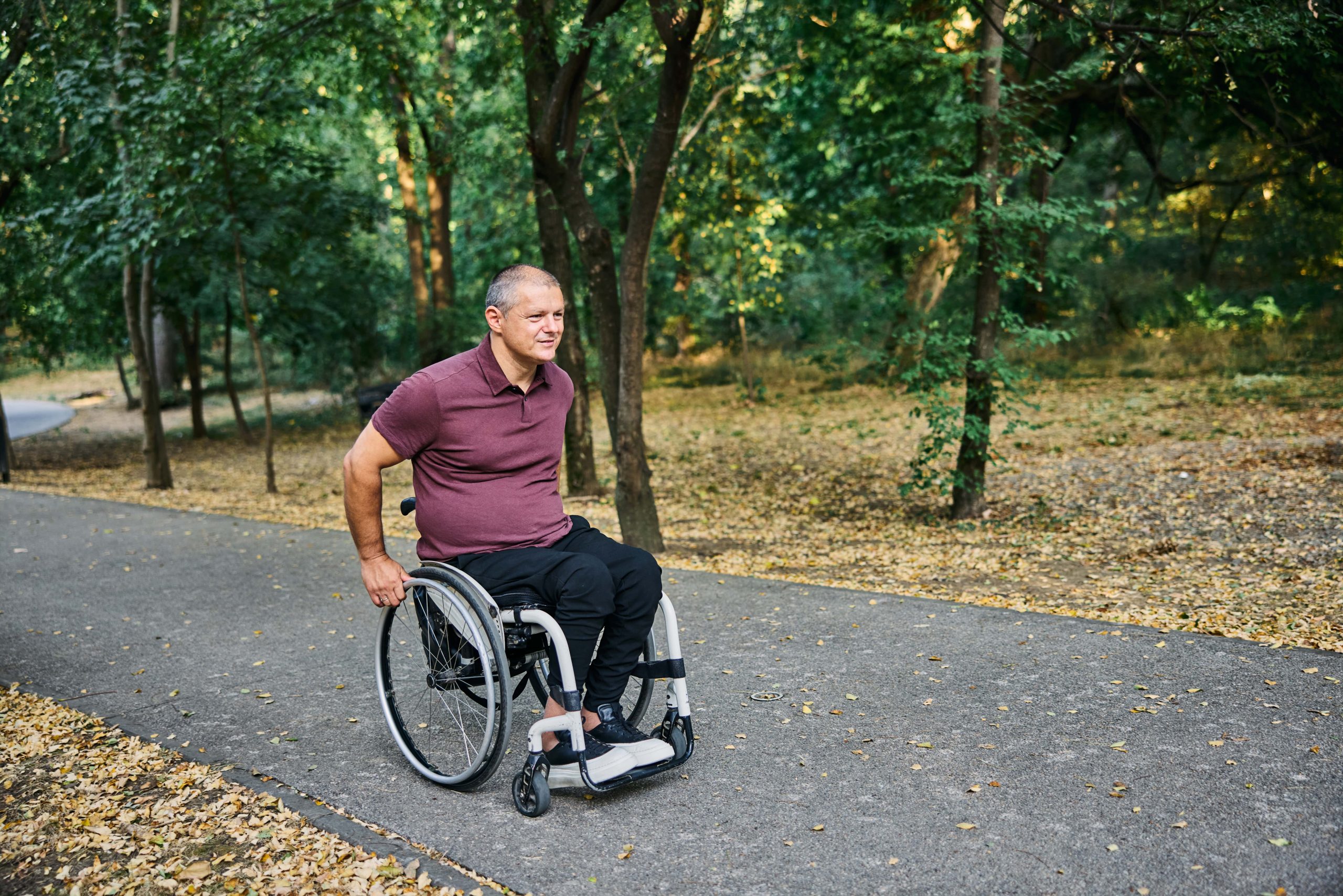 Un homme en fauteuil roulant sur un sentier entouré d’arbres Un homme en fauteuil roulant sur un sentier entouré d’arbres