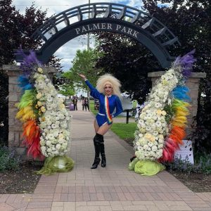 Une drag queen se tient debout devant l’entrée d’un parc. Une drag queen se tient debout devant l’entrée d’un parc.