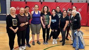 A group of smiling women standing on a basketball court.