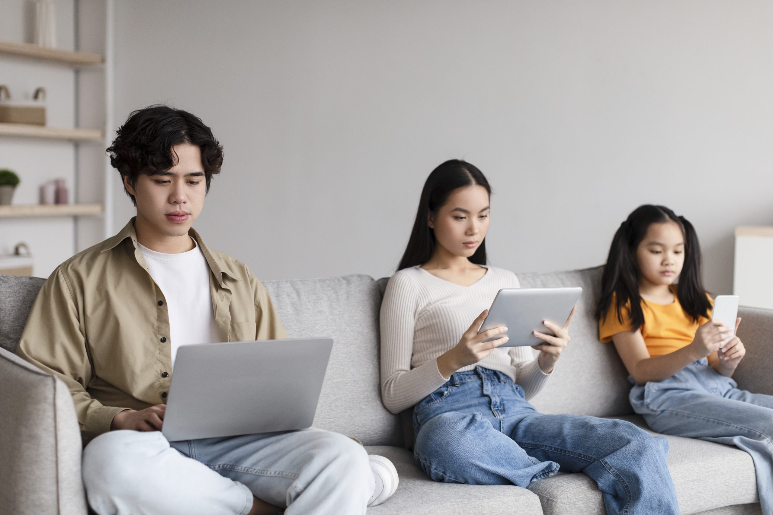 A group of teenagers using electronic devices on a couch. How much screen time is too much for teens? 7 ways to reduce it