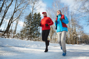 Deux personnes font leur jogging sur un sentier enneigé et entouré d’arbres.