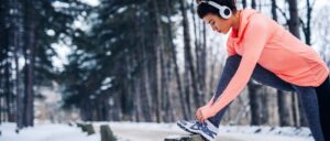 A woman tying a her shoe in a forest during winter. She has been goal setting.