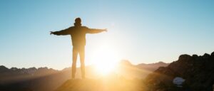 man standing in nature with arms spread triumphantly at sunset