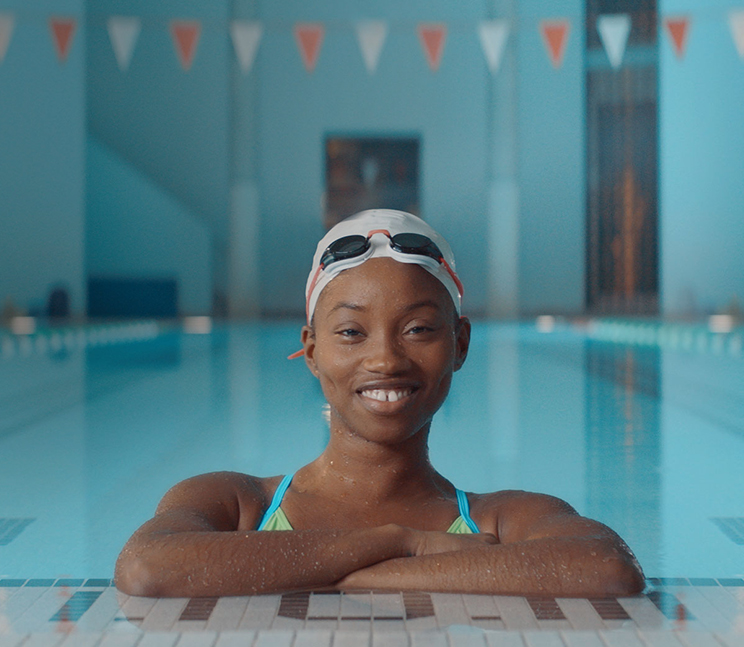 A teenage girl in a swimming cap and bathing suit smiling in pool