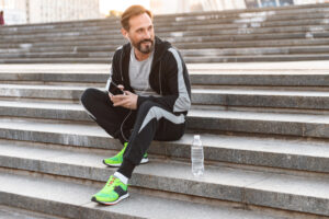 A man in workout clothes sitting on stairs while listening to music. 