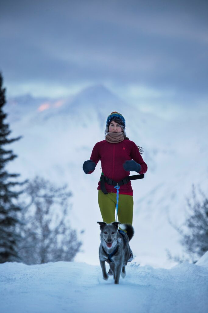 woman running in the snow with a dog