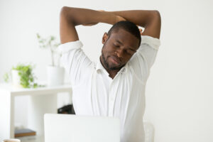 A man stretching his arms while sitting in front of a computer.