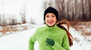 A smiling woman jogging on a snow-covered nature trail.