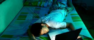 teen boy sleeps on his bed in front of a laptop