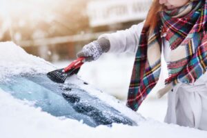 A person scraping snow off a car windshield. 