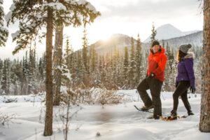 Two people snowshoeing on a nature trail with trees and mountains in the background