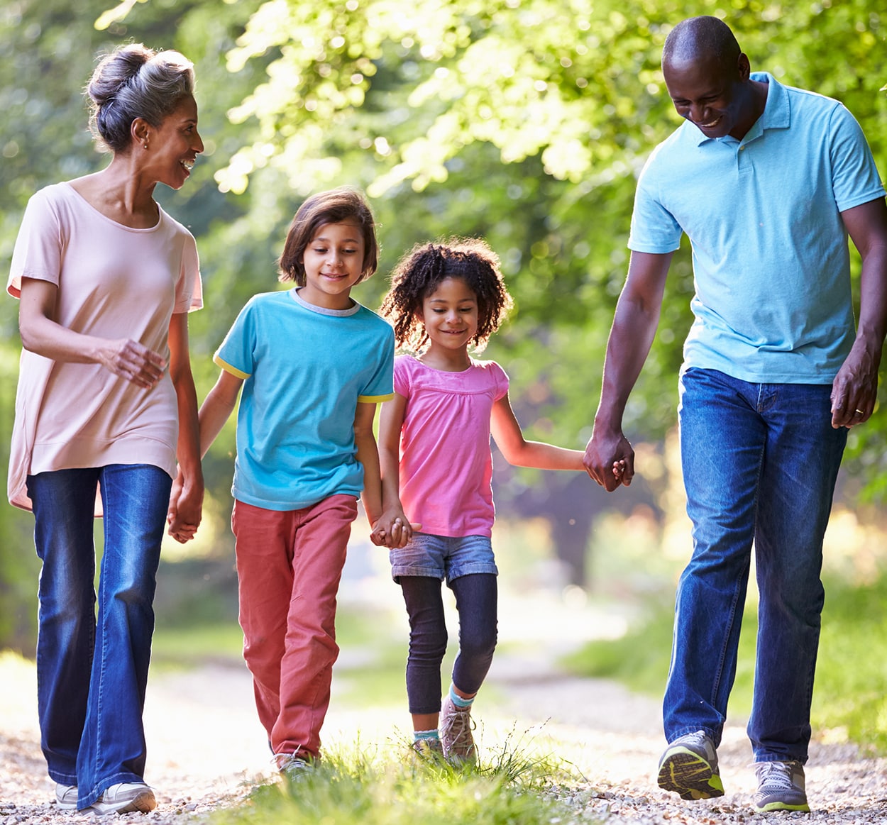 A man and woman holding hands with their two children, a girl and a boy, while walking through a forest