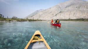 Deux personnes faisant du canot sur un lac avec des arbres et des montagnes en arrière-plan. 