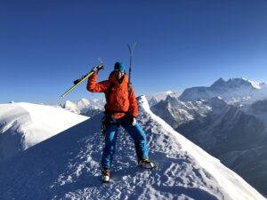 Jill Wheatley standing on Mera Peak (6,476 metres) in Nepal with Everest in the background while carrying skis and ski poles. She is overcoming adversity. 