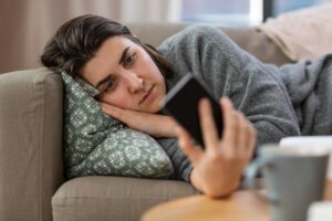 Allongée sur un canapé, une femme regarde son téléphone en fronçant les sourcils.