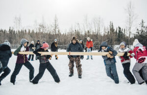 Un groupe de jeunes s’adonne au jeu déné de la poussée du poteau, un sport qui est joué aux jeux d'hiver de l'arctique, sur un terrain enneigé.