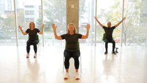 Three people sitting on chairs with their arms up in the air. 