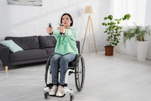 A woman in a wheelchair lifting a pair of dumbbells. 