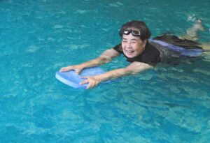 A smiling woman swimming in a pool, one of many key habits for a healthy heart. 