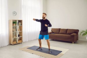 Dans un salon, un homme vêtu d’un ensemble d’entraînement boxe dans le vide. 