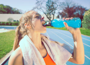 Une femme consomme une boisson sportive sur une piste de course extérieure. 