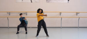 A person dancing in a chair beside a person dancing while standing up.