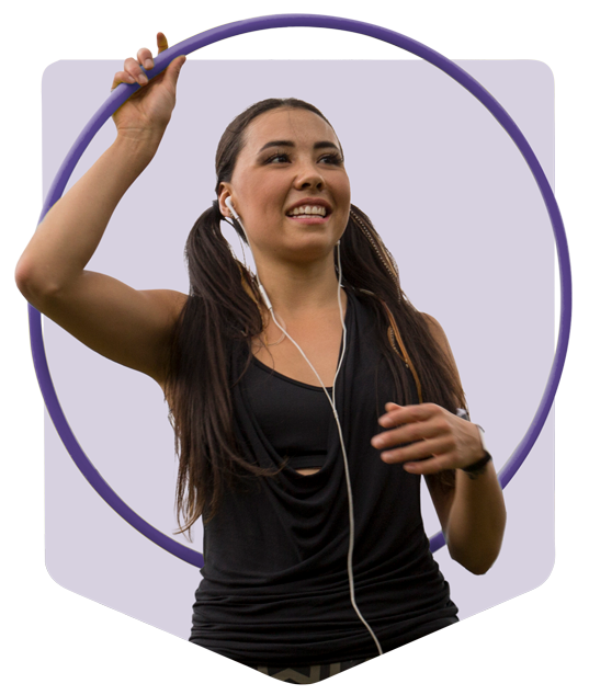 A young woman listening to music through earphones while playing with a hula hoop.