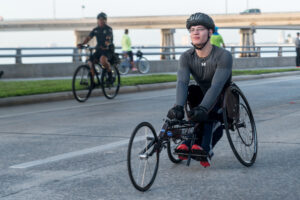 A man riding a handcycle on a road beside a person riding a conventional bicycle. 