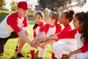 A man coaching a group of young girls on a baseball field. 