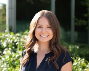 Katie Disimino smiling while standing in front of a bush outdoors.