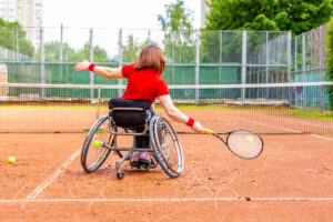 A woman playing wheelchair tennis on an outdoor clay court.