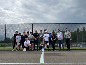 A group of people standing on a tennis court while holding pickleball racquets.