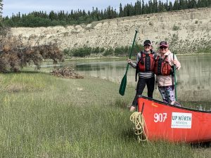 Madison and her mom standing next to a canoe in front of a river.