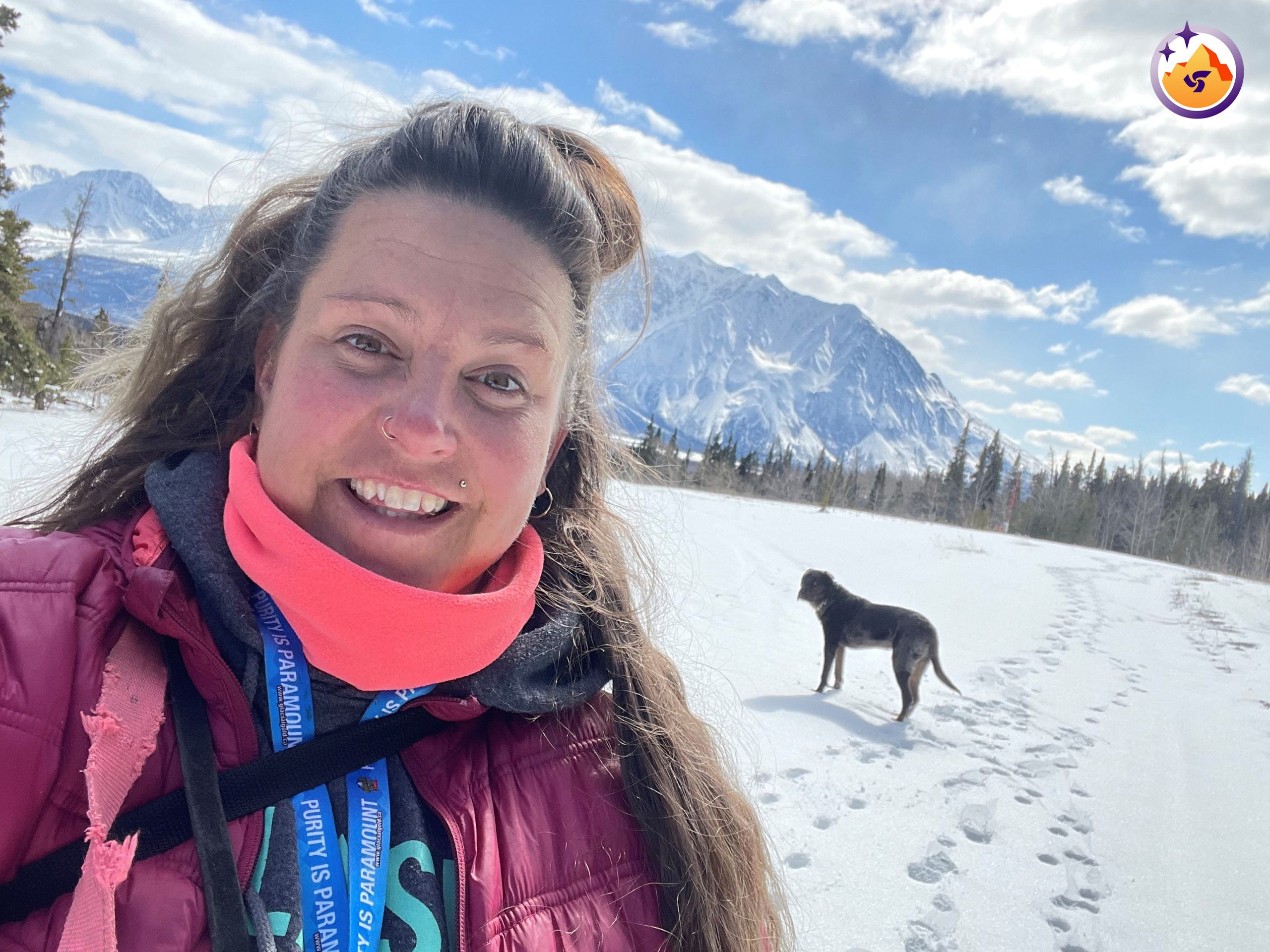 Isabelle Piché standing in a snow-covered field with a dog and mountain behind her.