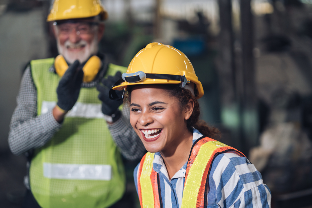 Deux ouvriers de la construction souriants portent des casques et des gilets de sécurité.