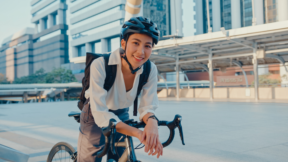 Une femme en tenue de travail assise sur un vélo dans un stationnement urbain.