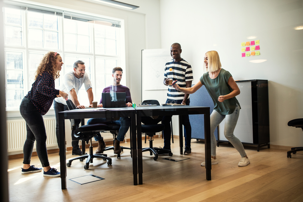 A group of people playing table tennis in an office meeting room. They're having an active workday.