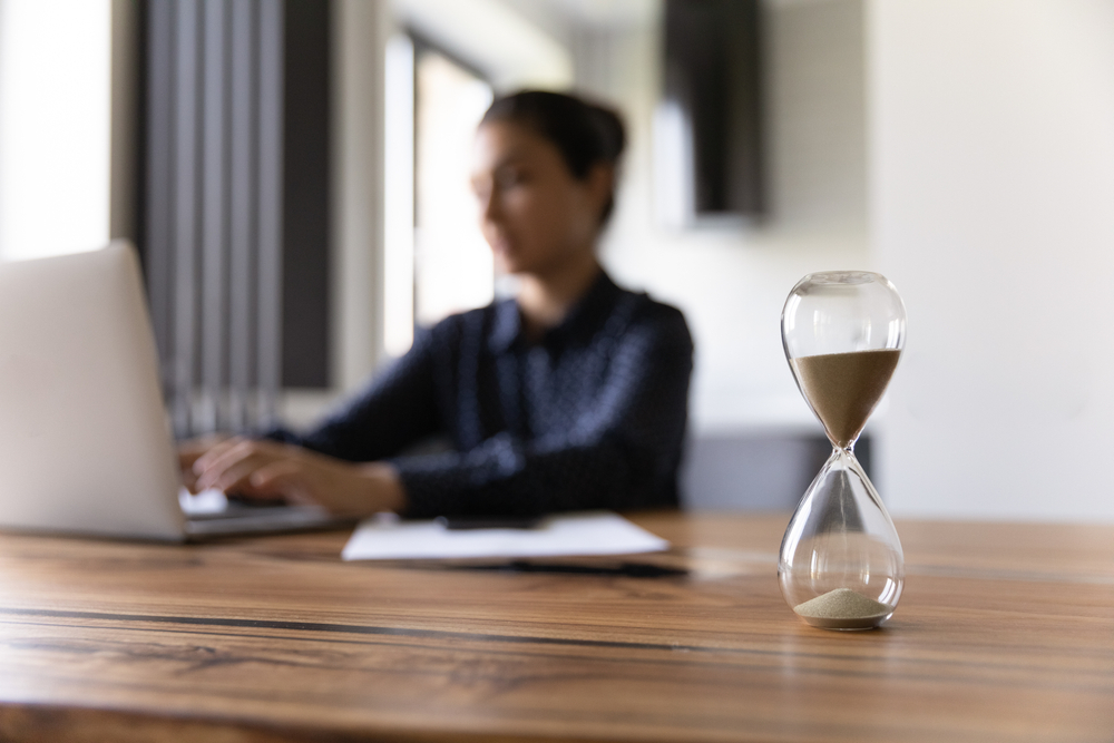 An hourglass beside a person typing on a computer. 