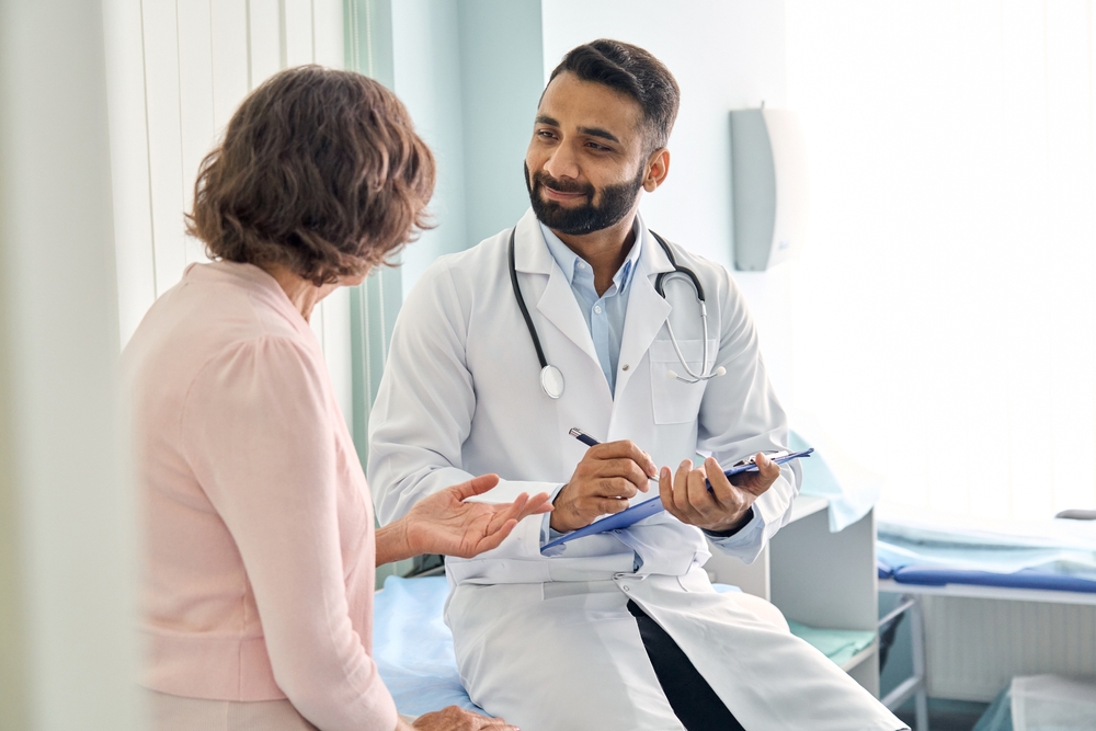 A male doctor talking to a female patient while taking notes.