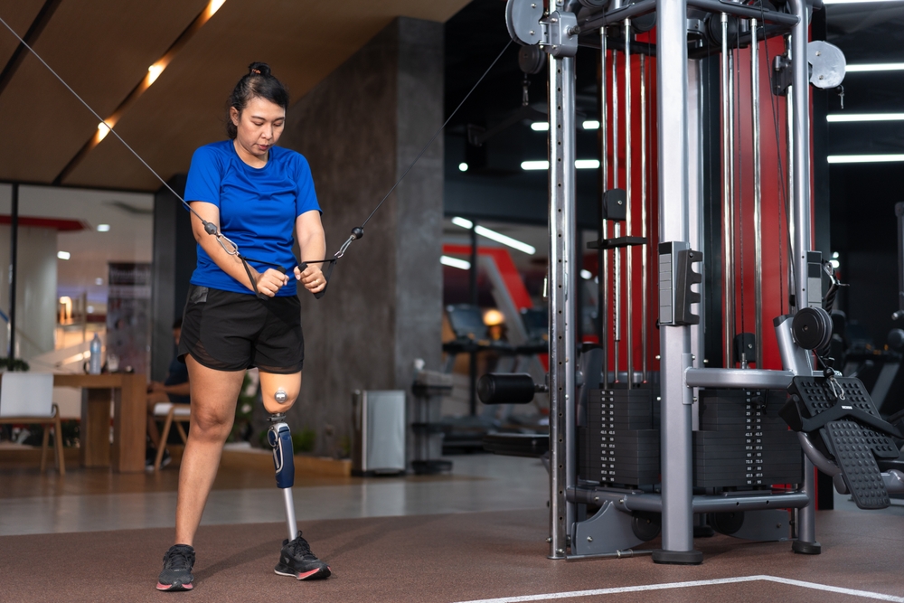 Une femme avec une prothèse de jambe se sert d’un appareil d’exercice dans une salle de sport.