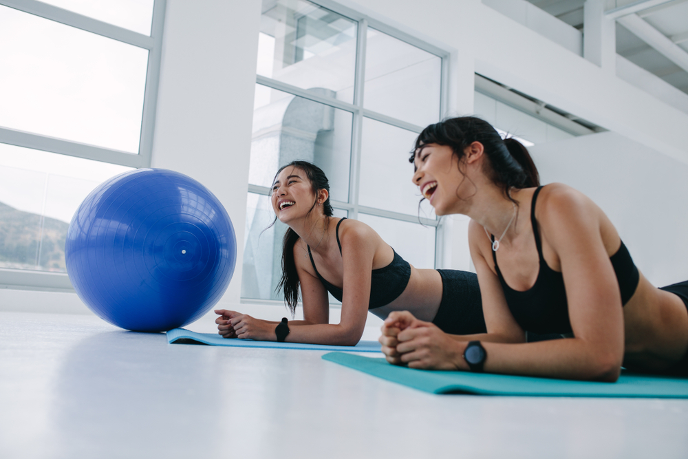 Deux femmes allongées sur des tapis de yoga à côté d’un ballon d’exercice rient. Deux femmes allongées sur des tapis de yoga à côté d’un ballon d’exercice rient.
