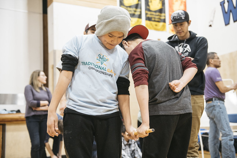 Two boys playing the Dene game called stick pull in a gymnasium. Two boys playing the Dene game called stick pull in a gymnasium.